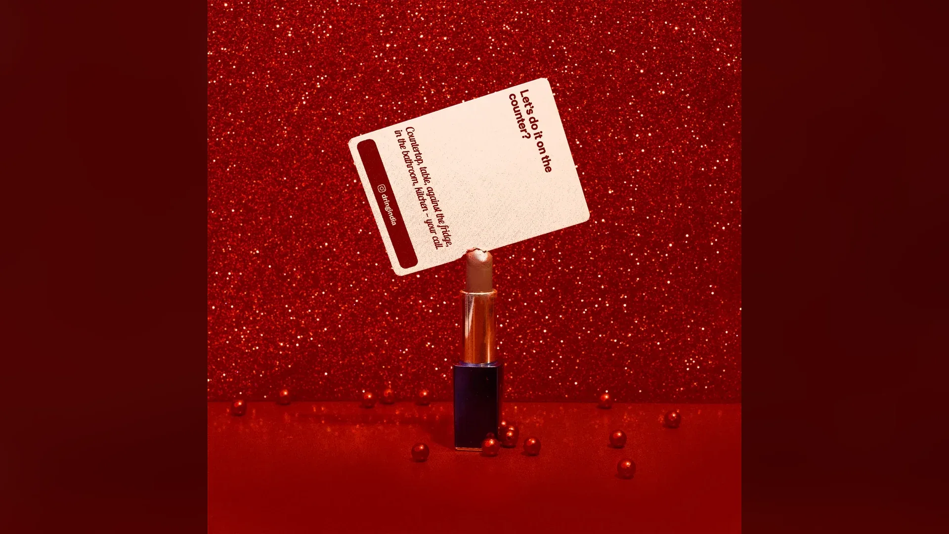 Naughty Dares campaign — card balanced on a lipstick against red glitter